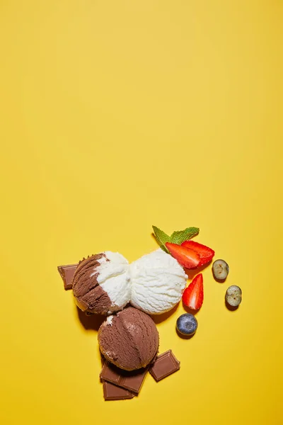 黄色の背景にベリーとチョコレートとミントとおいしい茶色と白のアイスクリームのトップビュー — ストック写真