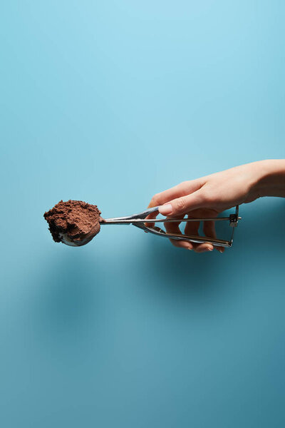 cropped view of woman holding scoop with chocolate ice cream on blue background