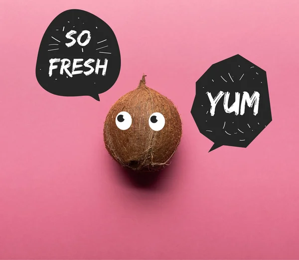 stock image top view of whole coconut with illustrated eyes on pink background with so fresh and yum lettering in black speech bubbles