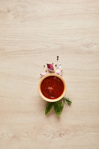 木のテーブルの上のハーブやスパイスの近くのボウルにおいしいトマトソースのトップビュー — ストック写真