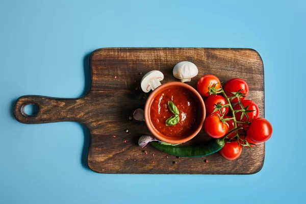 青い背景に新鮮な熟した野菜と木の板の上のボウルにおいしいトマトソースのトップビュー — ストック写真