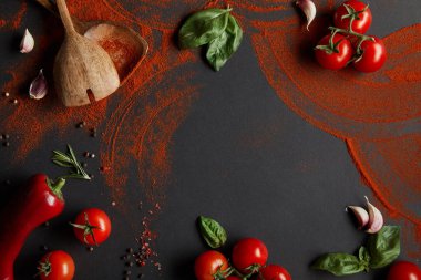 top view of red cherry tomatoes, garlic cloves, paprika powder, basil leaves and rosemary on black clipart