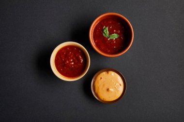 Domates ve hardal soslu siyah kaselerin üst görüntüsü.