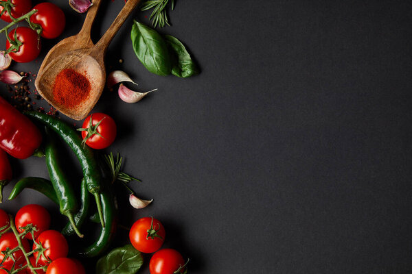 top view of cherry tomatoes, garlic cloves, fresh rosemary, peppercorns, basil leaves and green chili peppers on black