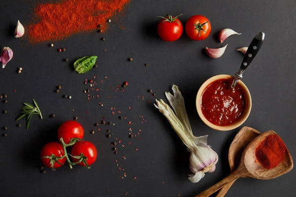 Top view of red cherry tomatoes, garlic cloves and fresh herbs near wooden spoons with paprika powder on black — Stock Image Top View Red Cherry Tomatoes Garlic Cloves Fresh Herbs Wooden Stock Photo