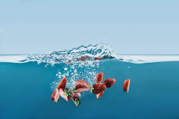 Pieces of strawberries falling into water with splashes — Stock Photo