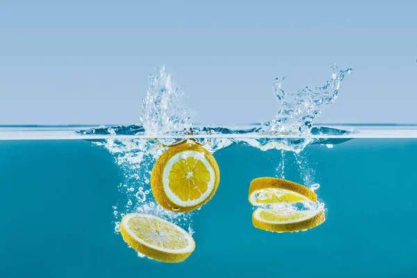 Fette di limone che cadono in acqua con spruzzi — Foto stock