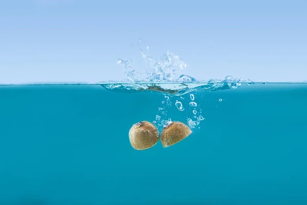 Kiwi halves falling into water with splashes — Stock Photo