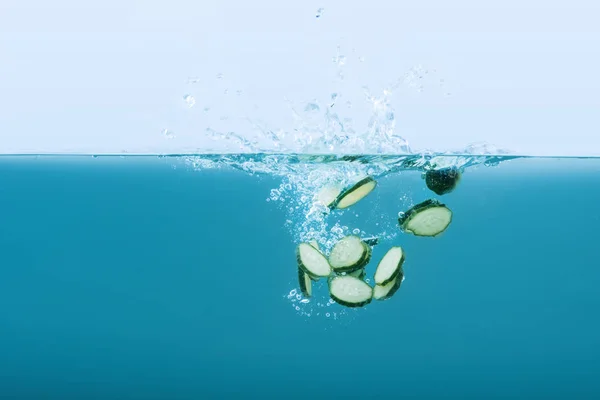 Gurkenscheiben fallen mit Spritzern ins Wasser — Stockfoto