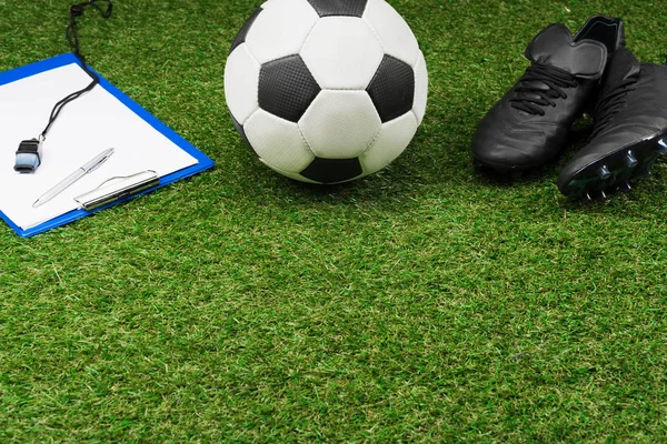 Буфер обмена с футбольным мячом и сапогами на траве — стоковое фото