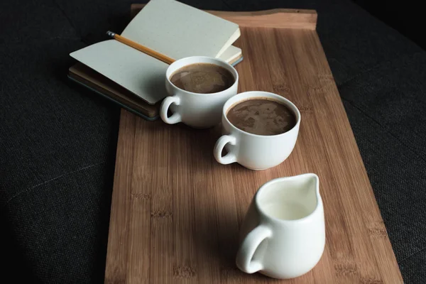 Café, jarra de leche y cuaderno en bandeja - foto de stock