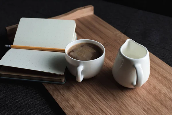 Café, jarra de leche y cuaderno en bandeja - foto de stock