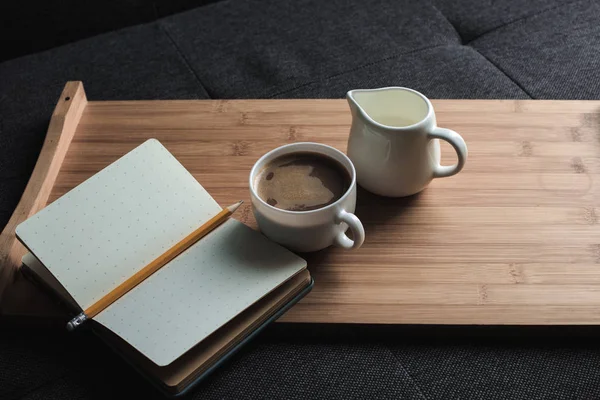 Café, jarra de leche y cuaderno en bandeja - foto de stock