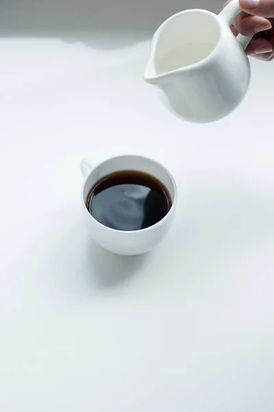 Verser du lait dans une tasse de café noir — Photo de stock