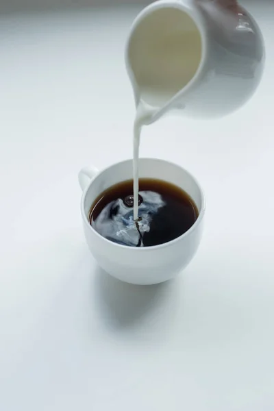 Verter leche en una taza de café negro - foto de stock