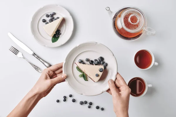 Mujer sirviendo tarta de queso con arándanos en la mesa - foto de stock