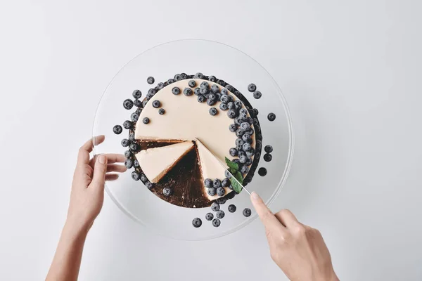 Woman slicing cheesecake with blueberries — Stock Photo