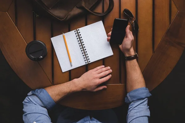 Homme avec bloc-notes ouvert en utilisant un smartphone — Photo de stock