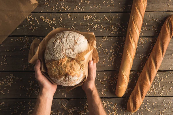 Loaf of bread in hands and baguettes — Stock Photo