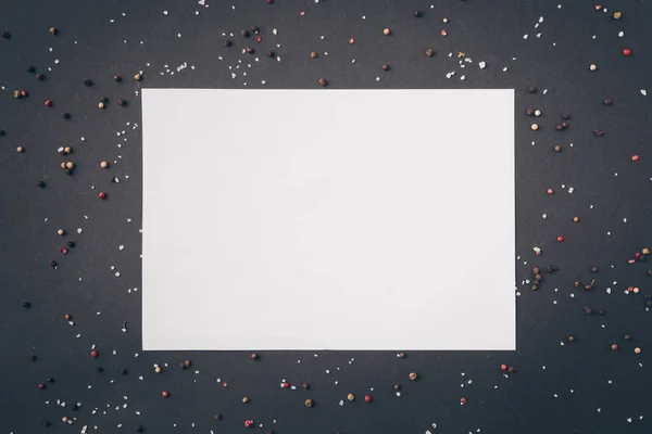 Top view of white sheet of paper among scattered pepper on gray table — Stock Photo