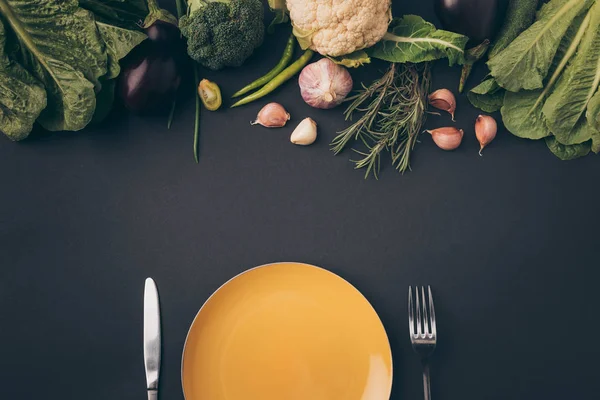 Top view of knife, fork and plate with vegetables on gray surface — Stock Photo