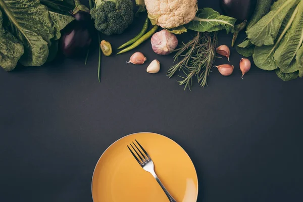 Top view of fork on plate and vegetables on gray table — Stock Photo