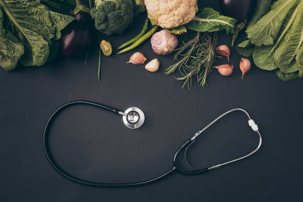 Top view of stethoscope with green vegetables on gray table — Stock Photo