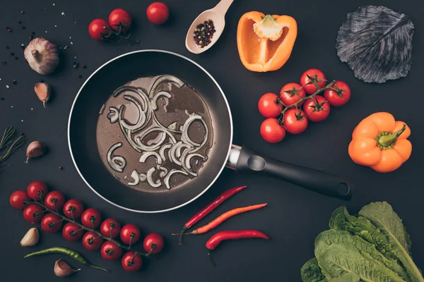 Vista superior da panela de ato de fritar com cebola entre verduras na mesa cinza — Fotografia de Stock