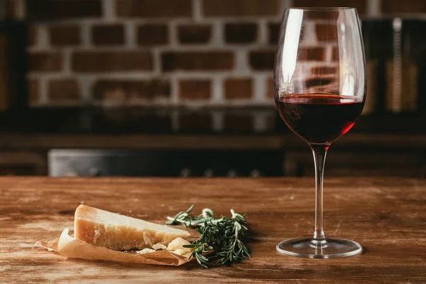 Copa de vino tinto, queso parmesano y romero fresco sobre mesa de madera - foto de stock