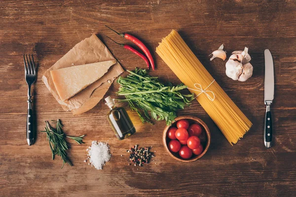 Vue du haut des pâtes en rangée, ingrédients frais, parmesan, fourchette et couteau sur table en bois — Photo de stock