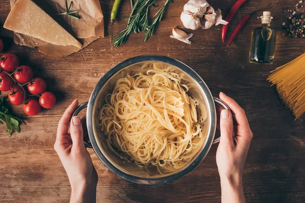 Vista superior de mãos com macarrão de espaguete e ingredientes em mesa de madeira — Fotografia de Stock