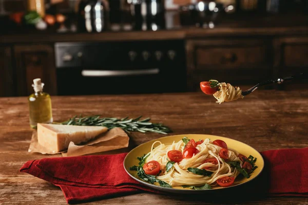 Delicious italian pasta with tomatoes and arugula in plate on table with Parmesan and rosemary — Stock Photo