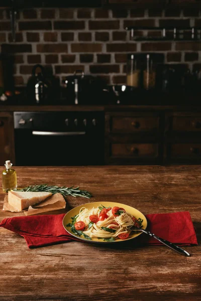 Traditional italian pasta with tomatoes and arugula in plate on table with Parmesan and rosemary — Stock Photo