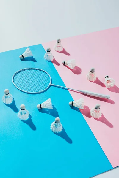 Shuttlecocks around badminton racket on blue and pink papers — Stock Photo