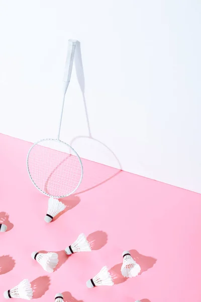 Бадминтонная ракетка и шаттлы на розовой бумаге у стены — стоковое фото