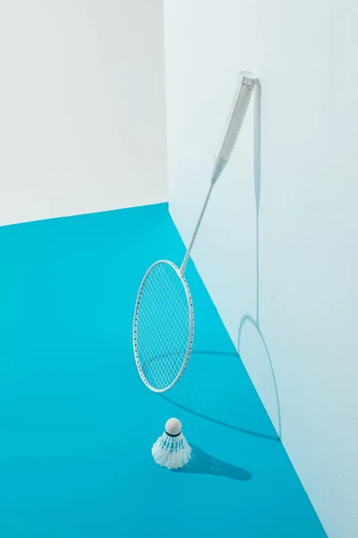 Raqueta de bádminton y volante sobre papel azul cerca de la pared blanca - foto de stock