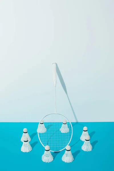 Raquete de badminton e shuttlecocks em papel azul perto da parede branca — Fotografia de Stock