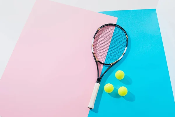 Vista superior de raqueta de tenis y bolas amarillas sobre papeles azules y rosados - foto de stock