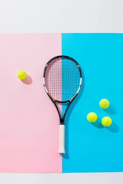 Draufsicht auf Tennisschläger und gelbe Bälle auf blauem und rosa Papier — Stockfoto