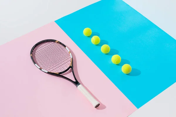 Тенісна ракетка на рожевих і жовтих м'ячах в ряд на синьому — стокове фото