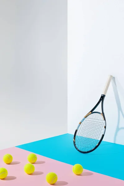 Palline da tennis gialle su carta rosa e racchetta da tennis blu a parete bianca con spazio copia — Foto stock