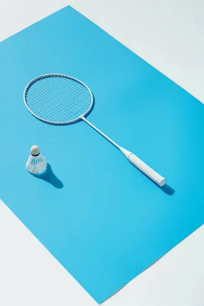 Raquette de badminton et volant couchés sur papier bleu, isolés sur blanc — Photo de stock