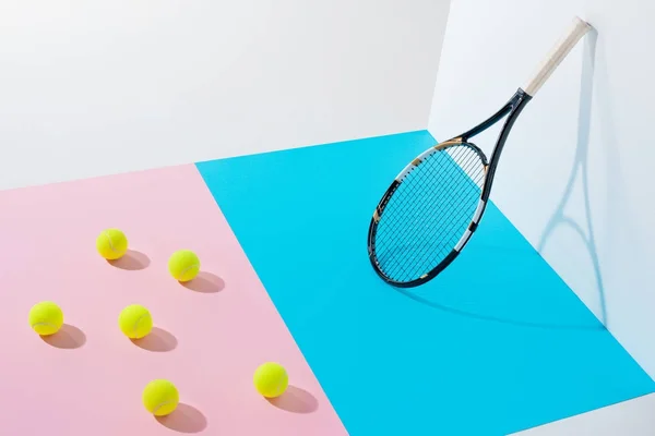 Yellow tennis balls on pink paper and tennis racket on blue at white wall — Stock Photo