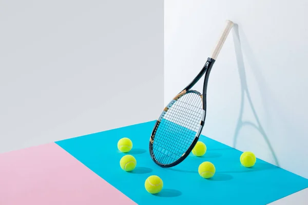 Yellow tennis balls on blue and pink papers and tennis racket at white wall — Stock Photo