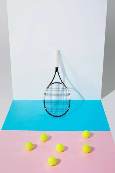Yellow tennis balls on blue and pink papers and tennis racket at white wall — Stock Photo