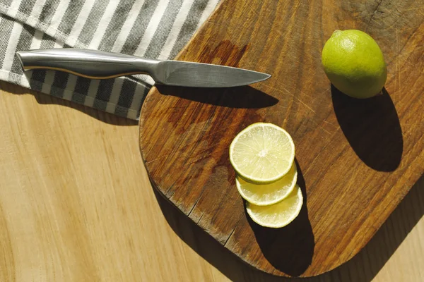 Top view of limes and knife on wooden board on table — Stock Photo