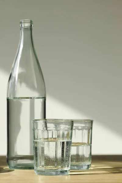 Bouteille transparente et verres avec eau minérale sur table en bois — Photo de stock