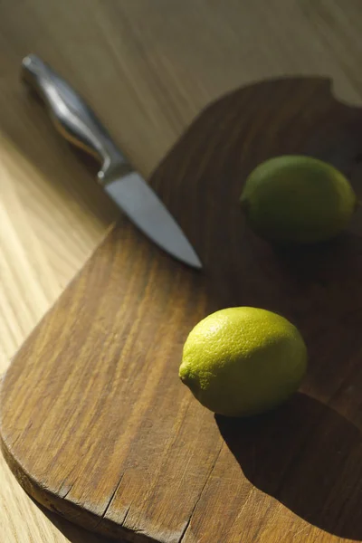 Overhead view of limes and knife on wooden board on tabletop — Stock Photo