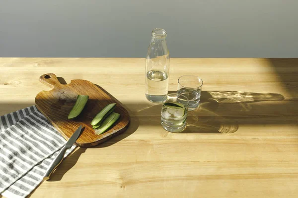 Vista aérea de pepinos cortados y botella con agua en mesa de madera - foto de stock