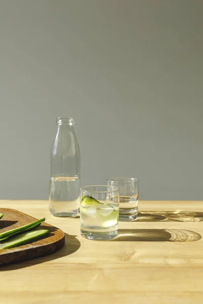 Pepinos cortados y agua mineral de desintoxicación en la mesa de madera - foto de stock
